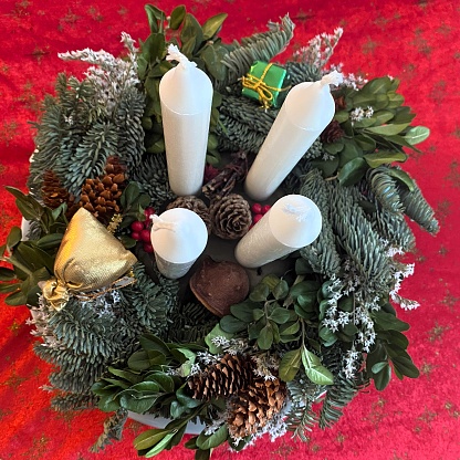 Two advent pillar candles burning for the second week of advent, in a dark room with copy space against a wood background with evergreen branches of an advent wreath.