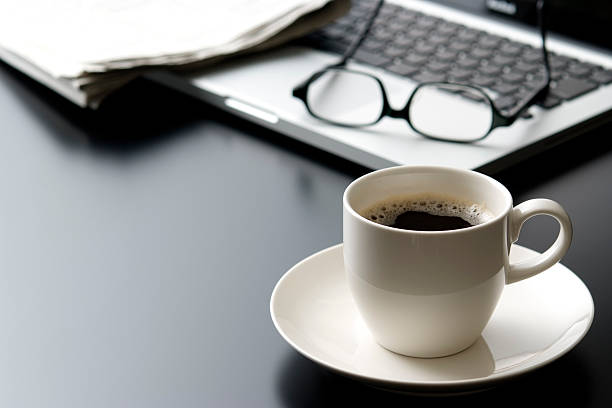 laptop e uma xícara de café na mesa de escritório - newspaper business close up nobody imagens e fotografias de stock