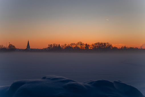 cold winter snow meadow covered in ice and foggy landscape at sunset