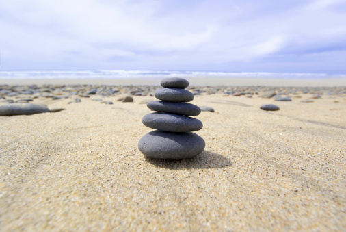 A stack of smooth rocks rests on the beach with the ocean in the background.