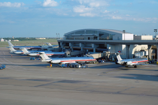 Silver planes sit on the ground at an airport terminal at the Dallas/Ft Worth International Airport.