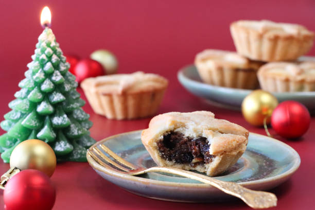 istock Close-up image of mince pie with missing bite on green plate with gold fork, green wax illuminated Christmas tree candle, gold and red baubles, red background, focus on foreground 1832667246