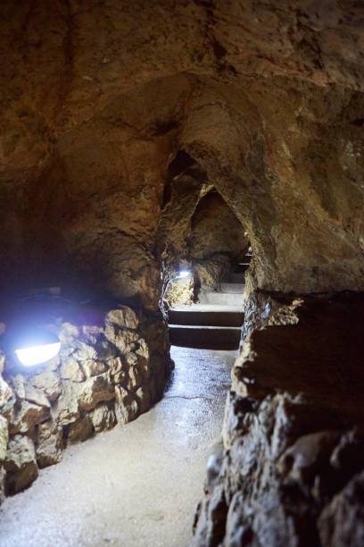 istock Dark cave view from inside with a lumen. Stalactites and stalagmites inside the stone grotto. Colorful stones in the cave. Lighting electricity beauty of the cave. 1832677097