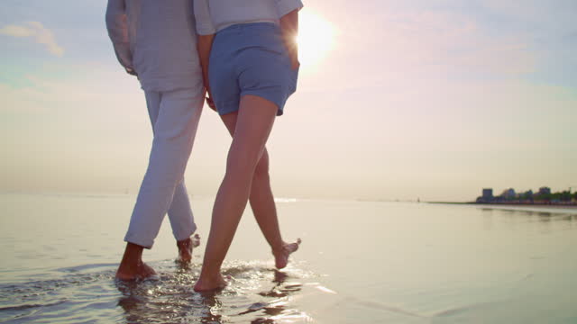 SLO MO TS Couple holding hands while walking barefoot on the sandy beach
