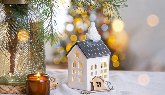 Key and tiny house of a small size on cozy home with Christmas decor on table of festive kitchen. Gift for New Year. Insurance, moving to new house, mortgage, rent and purchase real estate