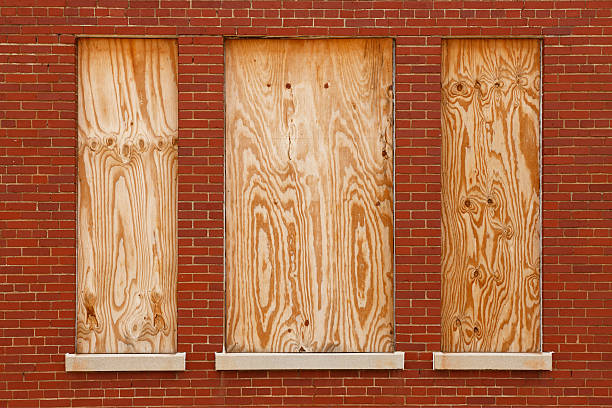 Boarded windows in abandoned building "Three windows in the brick wall of an abandoned building have been boarded up with plywood. Symmetrical image with central window flanked by two smaller windows.  Red brick, white concrete window sills. Image suitable for text on timber. Even lighting." boarded up photos stock pictures, royalty-free photos & images
