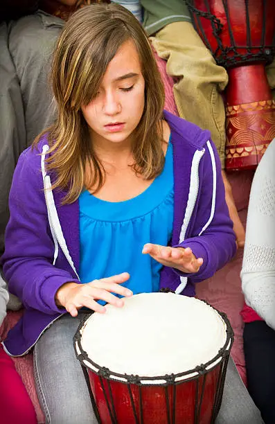 A young girl playing a Djembe drum in a music classroom.