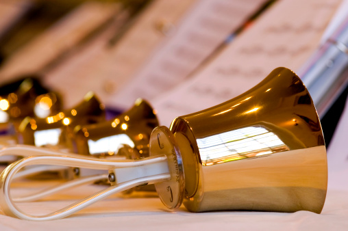 A row of polished brass handbells in front of sheet music on stands.