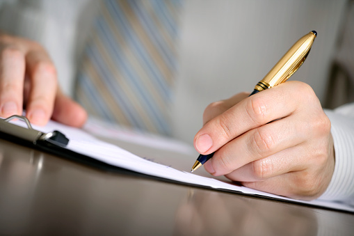 Close-up of a businessman's hand with a gilded pen writing something. Shallow depth of field.