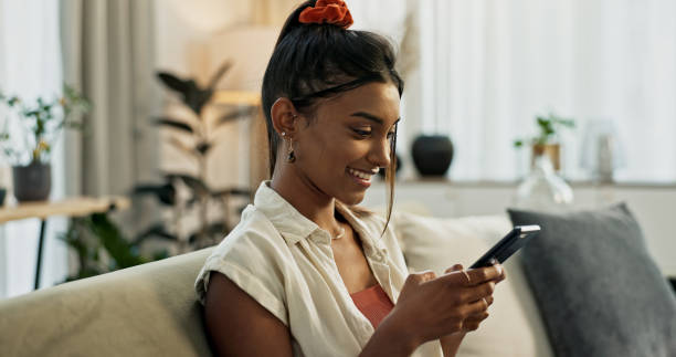 istock Woman, typing and smile with smartphone on sofa for social network, update multimedia subscription or chat at home. Happy indian girl, cellphone and download mobile games, reading notification or app 1832717266
