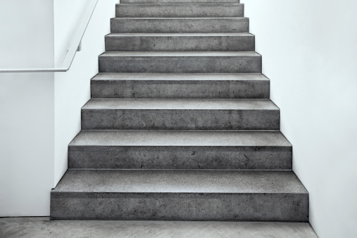 A staircase going up with natural wood steps and handrails, white risers, and wrought iron spindles.