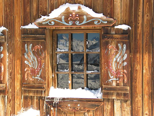 Vintage window of old wooden cabin mirrors winter landscape. Wooden rustic background. Reflections of trees and mountains in window glass.