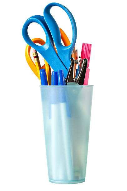 Fun Desk Organizer "A frosted plastic glass serves as a desk organizer with scissors, pencils,marker,pens and a hole punch on a white background." hole puncher stock pictures, royalty-free photos & images
