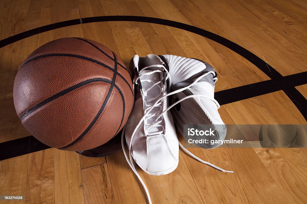 Pair of white basketball shoes next to basketball on court A basketball and shoes at center court. Basketball - Ball Stock Photo