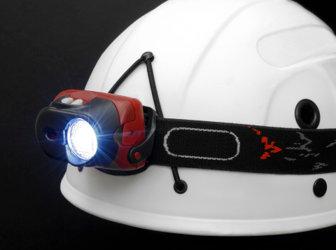 Close up on working headlamp on a white helmet isolated on black.