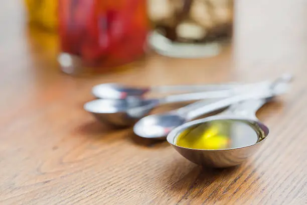 A measuring spoon of Olive Oil with bottle of flavored vinegar