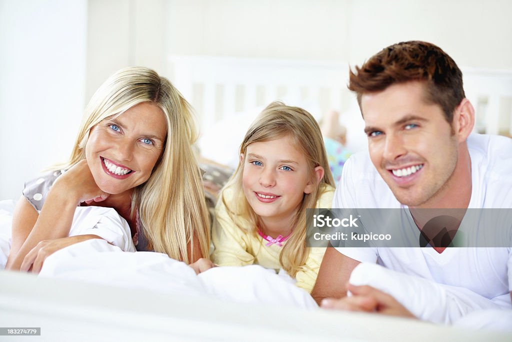 Sonriendo medio de pareja con su hija yacer en la cama - Foto de stock de 30-39 años libre de derechos