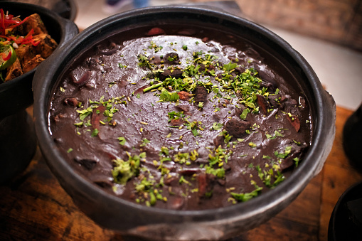 FEIJOADA served in a clay bowl on a rustic wooden table. Traditional Brazilian food