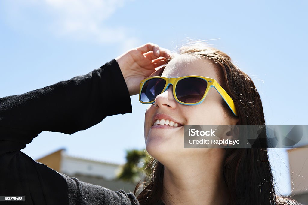 Smiling brunette in sunglasses shields eyes from bright sunlight This cute young brunette in sunglasses smiles as she shields her eyes from the bright sunshine of a summer's day. 20-29 Years Stock Photo