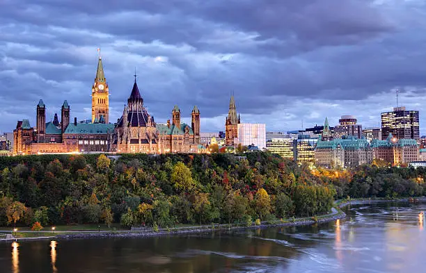 Parliament Hill atop a dramatic hill overlooking the Ottawa River in Ottawa, Ontario in autumn. Parliament Hill is home to Canada's federal government and is the centrepiece of Ottawa’s downtown landscape. Ottawa is known for is high-tech business sector, vast array of museums and high standard of living.