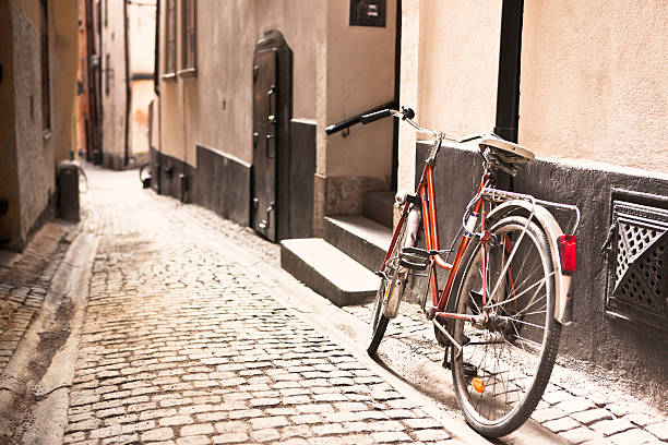 A red bicycle sits against a wall in a picturesque alley with cobblestone street in the old part of a European town.