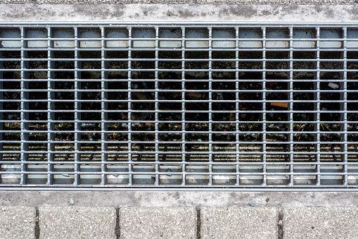 Gray metal grating with rectangular cells on a drainage channel on a railway platform.