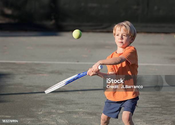 Young Boy Swinging A Tennis Racket At A Tennis Ball Stock Photo - Download Image Now