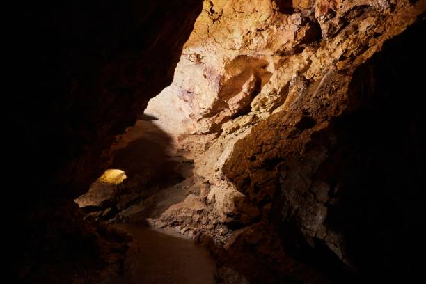 istock Dark cave view from inside with a lumen. Stalactites and stalagmites inside the stone grotto. Colorful stones in the cave. Lighting electricity beauty of the cave. 1832774658