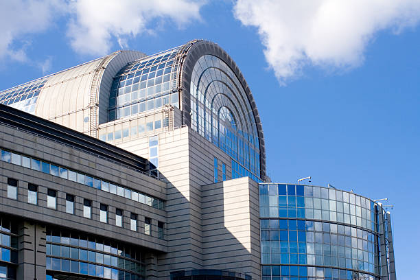 European Parliament building in Brussels "Side view of the stylish glass-covered European Parliament building in Brussels, against a blue, clouded sky." european parliament stock pictures, royalty-free photos & images