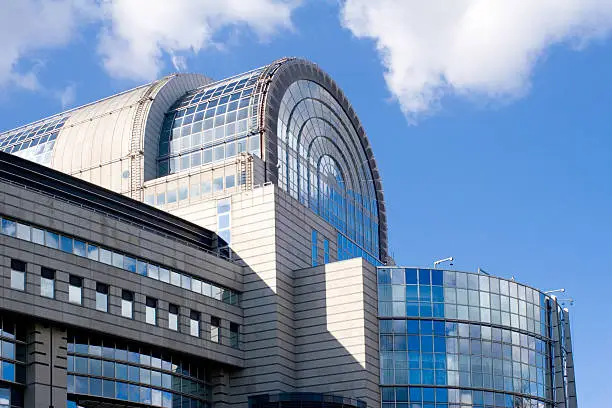 "Side view of the stylish glass-covered European Parliament building in Brussels, against a blue, clouded sky."