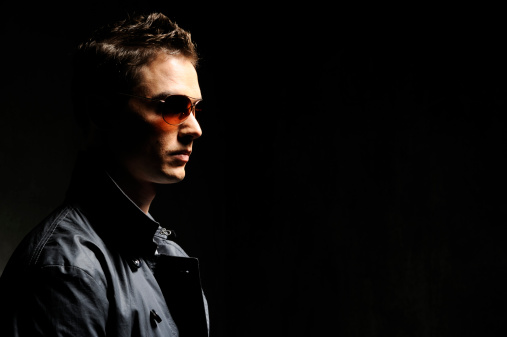 Profile of of a young man wearing sun glass in low key. Hair and makeup professionally done. Copy space.