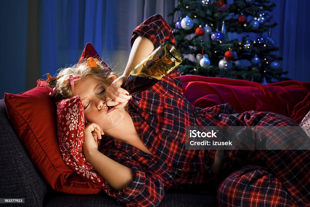 Sad Christmas "Young woman with curlers in hair wearing checkered pajamas lying on sofa and drinking wine. She is sad and lonely, Christmas tree in the background." 20-29 Years Stock Photo