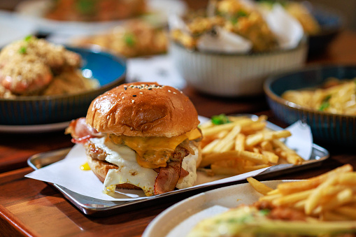A fresh and delicious burger, adorned with crispy french fries, elegantly presented on a rustic wooden board. This feast is laid out on the dining table in a restaurant, capturing the essence of both delectable food and a stylish lifestyle