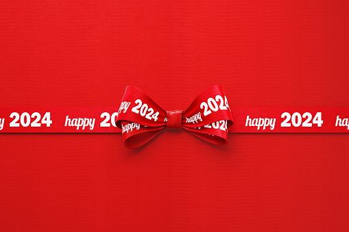 Happy 2024written red tied bow ribbon over red background. Horizontal composition with copy space. Happy 2024 concept.