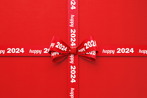 Happy 2024written red tied bow ribbon over red background. Horizontal composition with copy space. Happy 2024 concept.