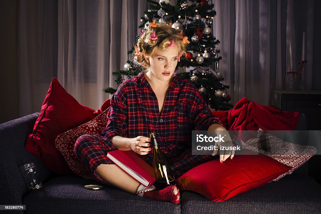 Sad and Lonely Christmas "Young woman with curlers in hair wearing checkered pajamas sitting on sofa and holding a bottle of wine. She is sad and lonely, Christmas tree in the background." 20-29 Years Stock Photo