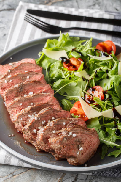 istock Beef tagliata with arugula, parmesan and cherry tomatoes is a delicious main course made with beef entrecote close-up on a plate. Vertical 1832823596