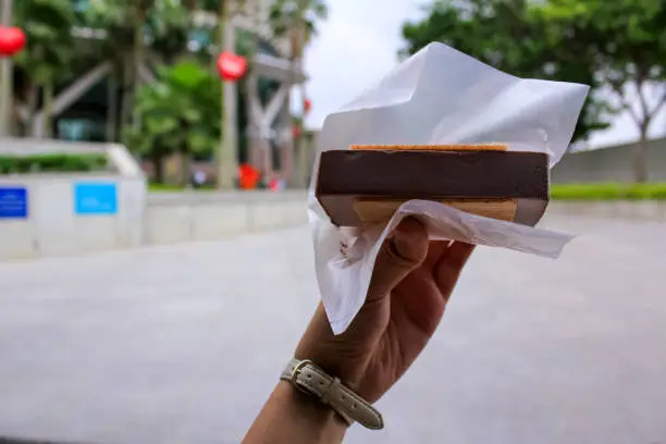 Photo of A woman hand holding an ice cream sandwich in the street.