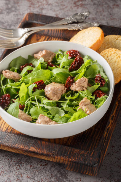 istock Cod liver salad with arugula and sun-dried tomatoes close-up in a bowl. Vertical 1832825683