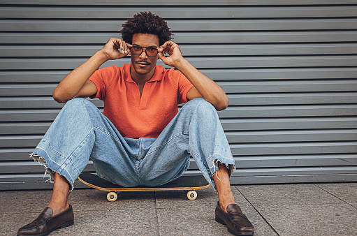 Modern you man sitting on skateboard on the sidewalk in city.