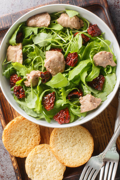 istock Appetizer balanced with canned cod liver, fresh arugula and sun-dried tomatoes served with toast close-up in a bowl on the table. Vertical top view 1832826764