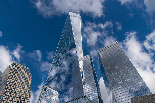 New York City, NY, USA-October 15, 2023; Low angle view of One World Trade Center with blue sky and white clouds reflected in the glass and steel façade of the building