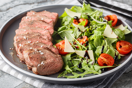Sliced Seared Steak Tagliata di Manzo served with arugula, cherry tomatoes and parmesan close-up in a plate on the table. Horizontal