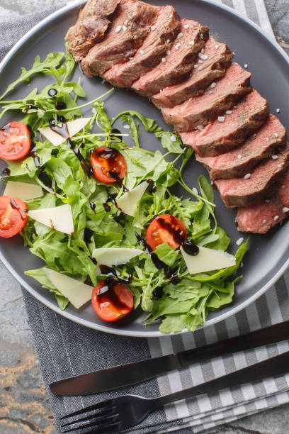 istock Beef tagliata with arugula, parmesan and cherry tomatoes is a delicious main course made with beef entrecote close-up on a plate. Vertical top view 1832829427