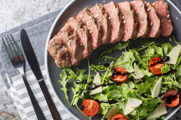 istock Beef steak tagliata with arugula, parmesan,  cherry tomatoes and balsamic close-up on a plate. Horizontal top view 1832829962