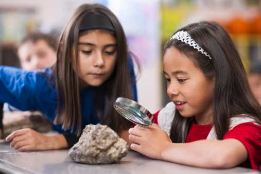 Elementary school children look at rocks with a magnifying glass.