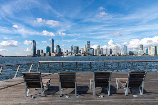 New York City, NY, USA-October 17, 2023; Chairs on Tide Deck of engineered rocky salt marsh on western edge of Pier 26 along the Hudson River with views on skyscrapers of Jersey City, New Jersey