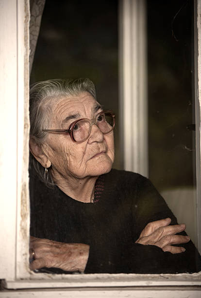 mulher idosa em pé e olhando pela janela fora - senior1 imagens e fotografias de stock