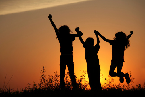 Silhouette of three happy young children jumping outside. Rural scene. Copyspace.