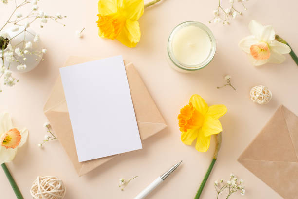 istock Send warm greetings for spring holidays with daffodils and gypsophila. Top view image showcases flowers, an envelope, and blank paper on a beige isolated background, perfect for adverts or text 1832851570
